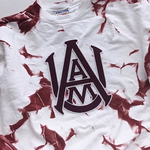 May include: White sweatshirt with a maroon tie-dye pattern and a maroon felt patch with the letters "A&M" in a vintage collegiate style.