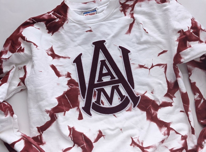 May include: White sweatshirt with a maroon tie-dye pattern and a maroon felt patch with the letters "A&M" in a vintage collegiate style.