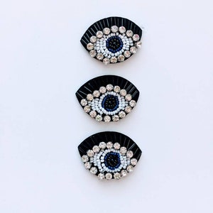 May include: Three black evil eye charms with white and blue beading. The charms are arranged vertically in a row.