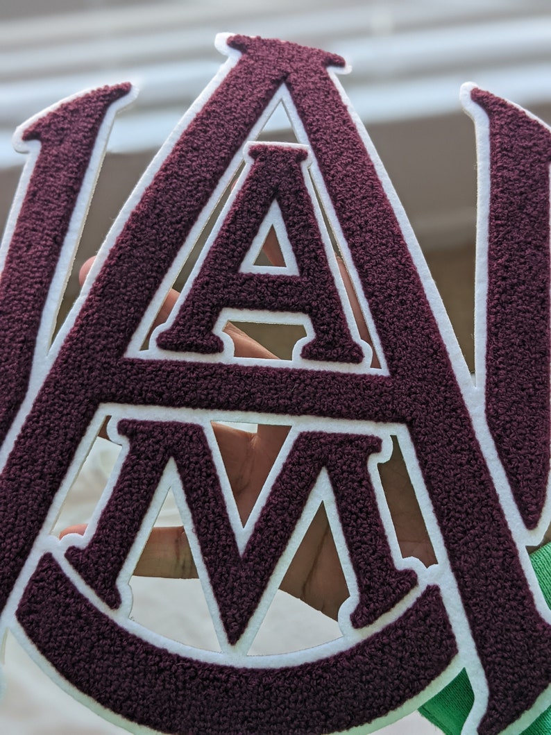 May include: A maroon felt patch with white outlines of the letters "A" and "M".