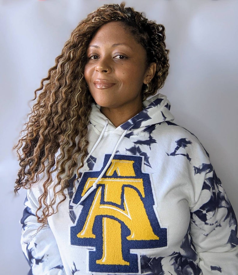 May include: White tie-dye hoodie with a large navy blue and gold embroidered letter "A" on the front.