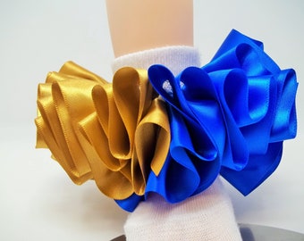 May include: A pair of white ankle socks with a gold and blue ribbon bow attached to the top. The ribbon is ruffled and layered.