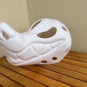 Op de afbeelding: Wit plastic masker met een tandenrij en gaten voor ogen en neus. Het masker is gevormd als een wolfskop.