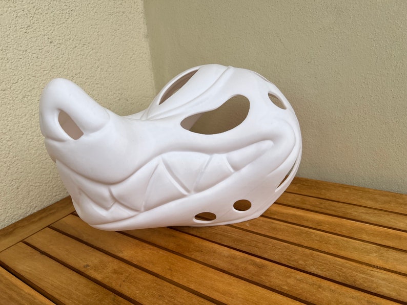 Op de afbeelding: Wit plastic masker met een tandenrij en gaten voor ogen en neus. Het masker is gevormd als een wolfskop.