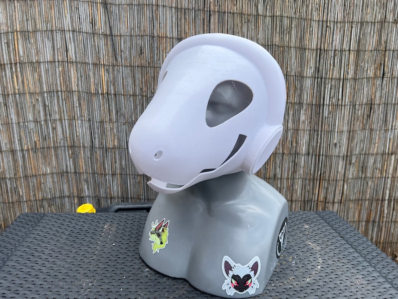 Pu&ograve; includere: Maschera di animale bianca stampata in 3D con una grande testa rotonda e una bocca larga e aperta. La maschera &egrave; su una testa di manichino grigia.