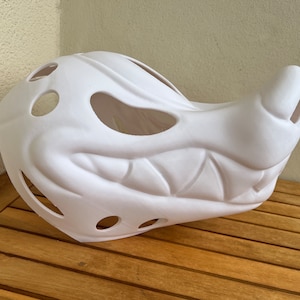 Op de afbeelding: Wit plastic masker met een tandenrij en gaten voor ventilatie. Het masker is ontworpen om op een grommend dier te lijken.