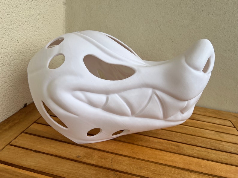 Op de afbeelding: Wit plastic masker met een tandenrij en gaten voor ventilatie. Het masker is ontworpen om op een grommend dier te lijken.
