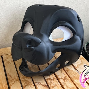 May include: A black, 3D-printed mask with white eye openings, resembling a canine or similar animal. The mask has a detailed snout, open mouth, and several small holes on top. The logo "LIQUID TOOTH" is visible in the lower right corner.