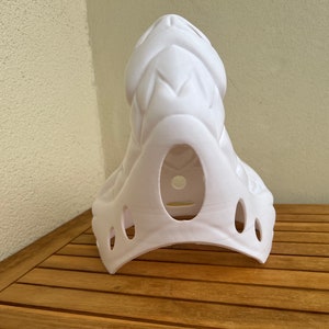Op de afbeelding: Witte plastic masker met een textuur, schubben ontwerp. Het masker heeft een grote opening voor het gezicht en verschillende kleinere gaten rond de randen.