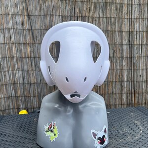 Pu&ograve; includere: Maschera in gesso bianco non verniciata con due grandi fori per gli occhi e un foro pi&ugrave; piccolo per la bocca. La maschera &egrave; su una testa di manichino grigia.