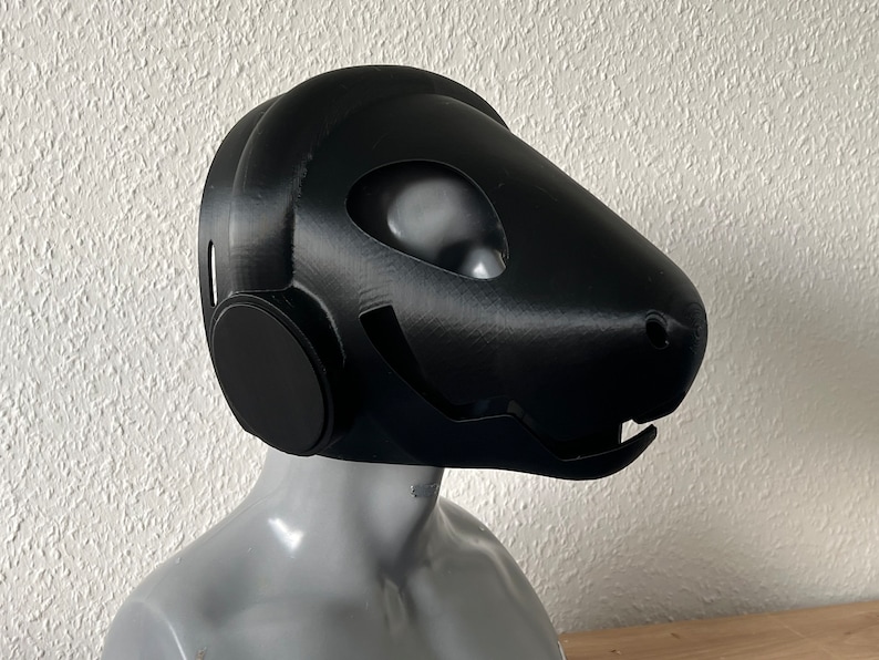 Pu&ograve; includere: Una maschera nera stampata in 3D con un design futuristico. La maschera ha un grande pezzo di testa arrotondato con un piccolo muso appuntito. La maschera ha un grande foro circolare per gli occhi su ciascun lato.