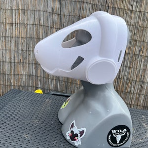Pu&ograve; includere: Maschera di pelliccia bianca con un grande orecchio rotondo bianco sul lato. La maschera &egrave; su un manichino grigio con un adesivo bianco e nero di un teschio con il testo "W.O.A.  ESTD. 2020 THANKS FOR YOUR SUPPORT" sul davanti.