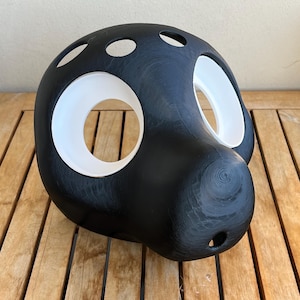 May include: A black and white mask with large, circular eye openings and smaller holes on top. The mask has a rounded shape and is made of a textured material. The eye openings are lined with white.