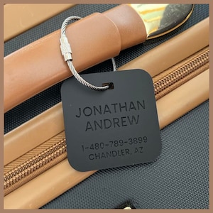 May include: Black luggage tag with a silver metal ring. The tag has the text "JONATHAN ANDREW" and "1-480-789-3899 CHANDLER, AZ" printed on it.