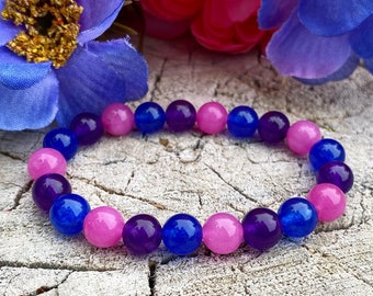 May include: A bracelet made of pink, purple, and blue beads. The beads are round and smooth, and they are strung together on a clear elastic cord.