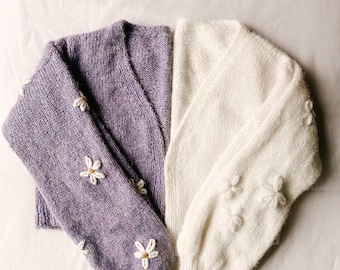 May include: Two knitted cardigans with floral embroidery. One cardigan is purple and the other is white.