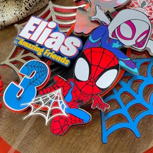 Pode incluir: Um conjunto de toppers para bolo vermelho, azul e branco com o Homem-Aranha, Spider Gwen e uma teia de aranha. Os toppers tamb&eacute;m incluem o nome "Elias" e a frase "and his Amazing Friends".