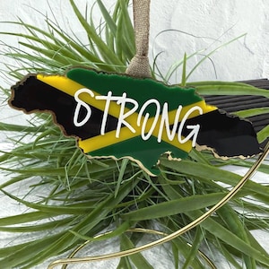 Peut inclure: Ornement décoratif en forme d'île, aux couleurs du drapeau jamaïcain : vert, jaune et noir. Le mot « STRONG » est écrit en blanc au centre. L'ornement est bordé d'or et possède un ruban en toile de jute pour l'accrocher.