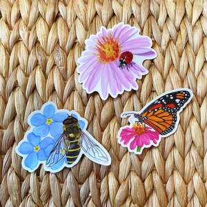 May include: Three colorful stickers featuring a bee on blue forget-me-not flowers, a butterfly on a pink flower, and a ladybug on a pink flower.