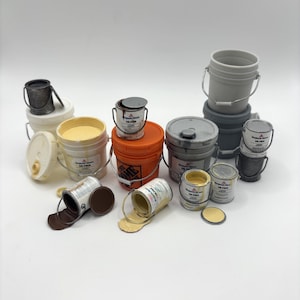 Può includere: Una collezione di mini barattoli e secchi di vernice di varie dimensioni e colori. Alcuni barattoli sono aperti, versando vernice. I colori includono bianco, arancione, grigio e giallo. Il testo "Benjamin Moore ULTRA" è visibile.