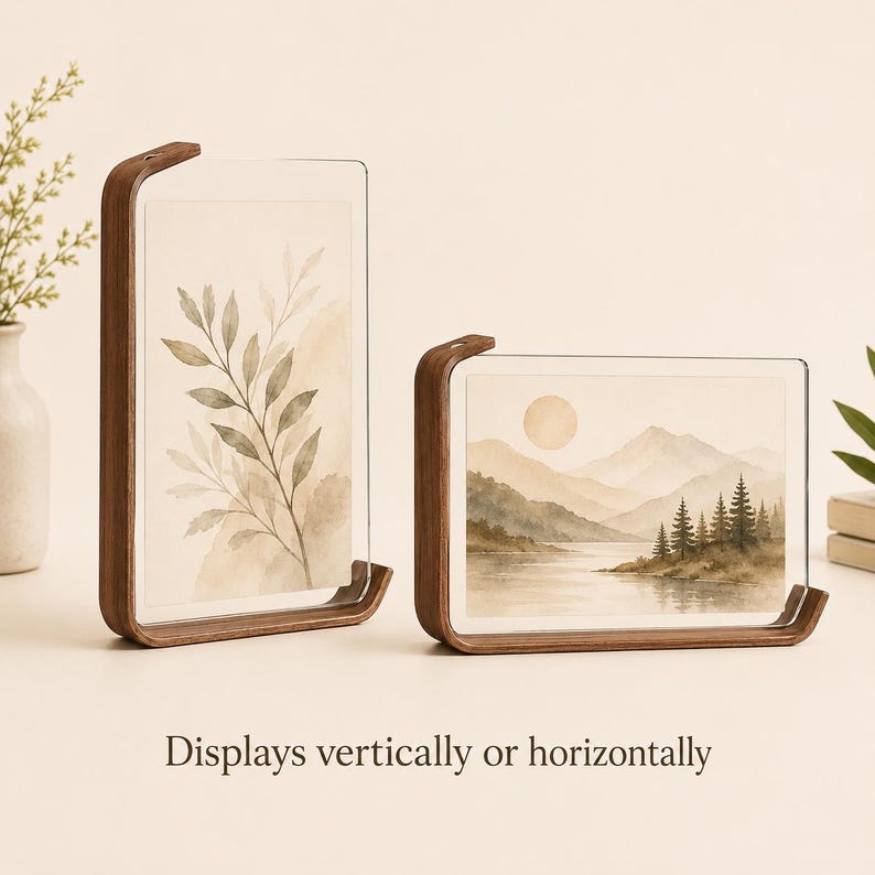 K&ouml;nnte beinhalten: Zwei Rahmen aus dunklem Holz mit klaren Acrylplatten, die Aquarellbilder halten. Ein Rahmen steht vertikal mit einer Blattillustration, der andere horizontal mit einer Berglandschaft. Der Text lautet: Displays vertically or horizontally.
