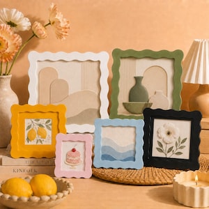 Puede incluir: Una colección de seis marcos de fotos cuadrados con bordes ondulados en blanco, verde oliva, amarillo, rosa, azul claro y negro. Los marcos contienen varias impresiones artísticas que incluyen formas abstractas, un limón, un pastel, olas y una flor.