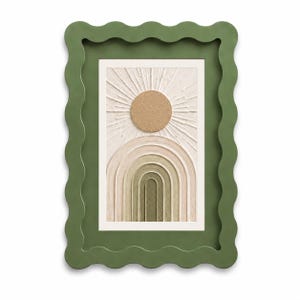 May include: A rectangular wall art piece featuring a textured beige sun and a series of concentric arches in shades of cream, tan, and olive green. The artwork is encased in a thick, matte olive green frame with a distinct wavy, scalloped edge.