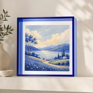 May include: A square wall art piece featuring a landscape painting of a blue-toned lake, rolling hills, and a small house, encased in a deep blue acrylic frame. The scene includes a field of white flowers in the foreground and distant mountains.