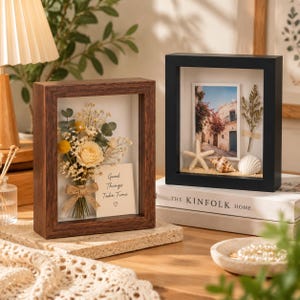 May include: Two shadow box frames, one dark wood and one black, displaying decorative items. The wood frame holds a dried flower bouquet and a card reading Good Things Take Time. The black frame contains a photo, a starfish, and seashells.