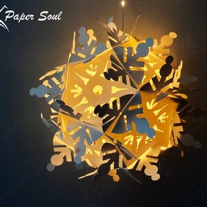 Peut inclure: Une lanterne en papier en forme de flocon de neige blanc avec une lumi&egrave;re &agrave; l'int&eacute;rieur, qui brille intens&eacute;ment. Le flocon de neige est compos&eacute; de plusieurs couches de papier, cr&eacute;ant un effet 3D. La lanterne est suspendue au plafond.