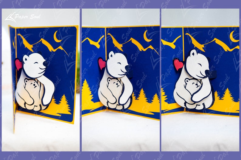 May include: A pop-up card featuring a white polar bear hugging a smaller white polar bear. The card has a blue background with yellow trees and mountains. The polar bears have red hearts on their chests.