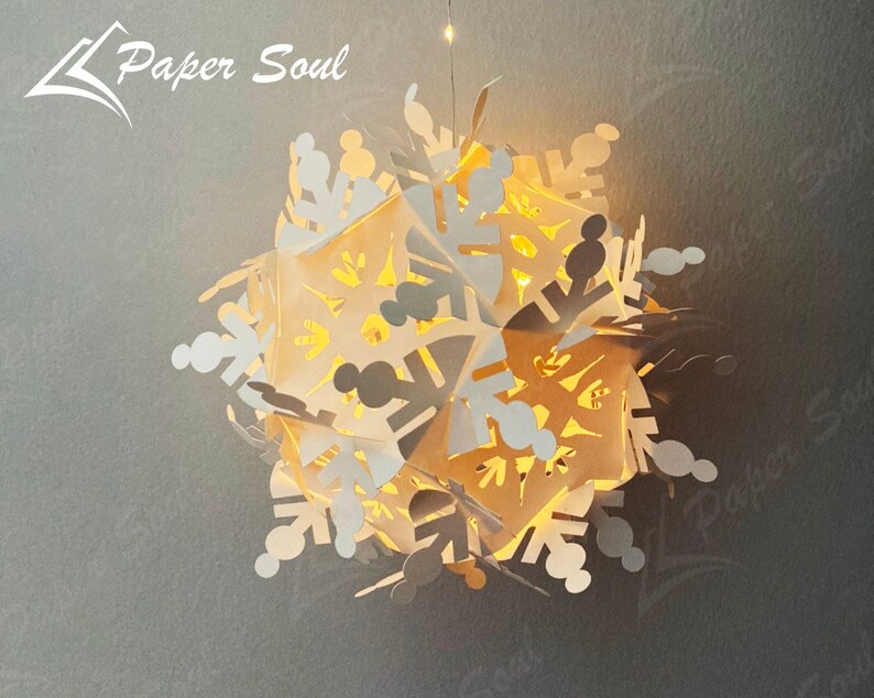 Peut inclure: Une d&eacute;coration de No&euml;l en forme de flocon de neige en papier blanc avec une lumi&egrave;re blanche chaude qui brille &agrave; travers les d&eacute;coupes complexes. Le flocon de neige est suspendu au plafond et le texte "Paper Soul" est visible dans le coin sup&eacute;rieur gauche de l'image.