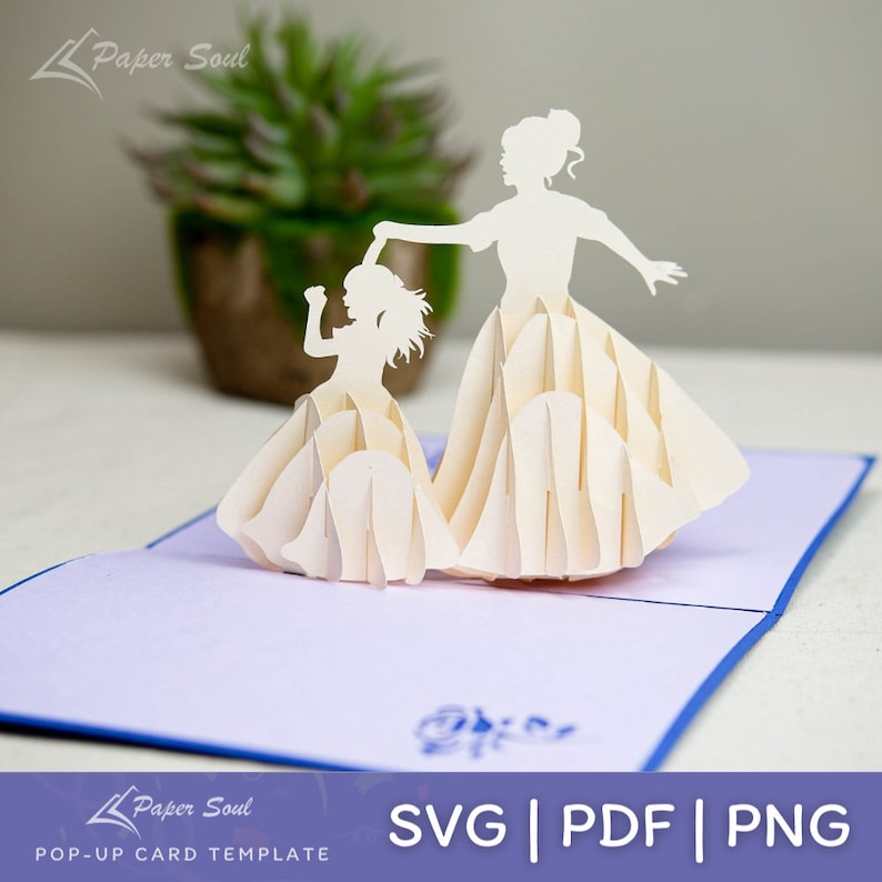 May include: A white pop-up card featuring a mother and daughter in silhouette, dancing together. The card is folded and has a blue border. The text "SVG | PDF | PNG" is printed on the bottom of the card.