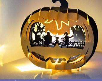 Może przedstawiać: Szablon trójwymiarowej karty pop-up w kształcie dyni z przerażającą sceną Halloweenową w środku. Karta jest wykonana z papieru i przeznaczona do wycięcia i złożenia. Scena wewnątrz dyni przedstawia nawiedzony dom, cmentarz i dzieci chodzące po cukierki.