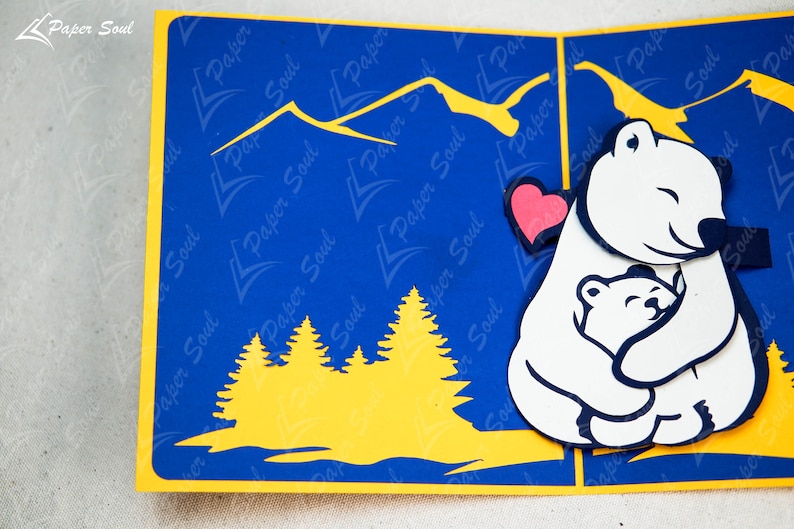 May include: A white polar bear with a red heart cutout holding a smaller white polar bear. The bears are against a blue background with yellow mountains and trees.