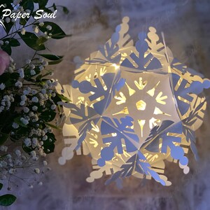 Peut inclure: Une lanterne en papier en forme de flocon de neige blanche avec une lumi&egrave;re &agrave; l'int&eacute;rieur. La lanterne est faite de plusieurs couches de papier et pr&eacute;sente un design d&eacute;licat et complexe. La lumi&egrave;re traverse le papier, cr&eacute;ant une lueur chaleureuse et accueillante.