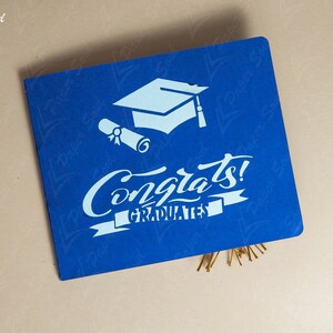 May include: A blue card with white text and a graduation cap and scroll design. The text reads "Congrats! Graduates".