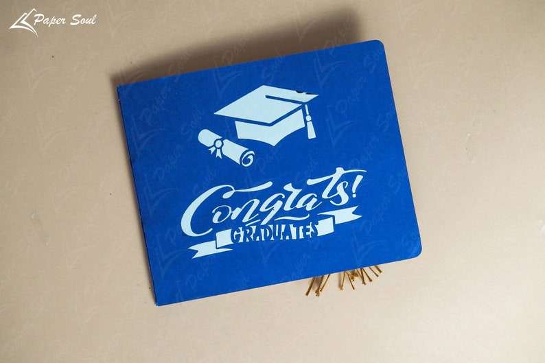 May include: A blue card with white text and a graduation cap and scroll design. The text reads "Congrats! Graduates".