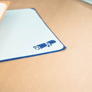 May include: A blue and white desk mat with a blue diploma icon in the center. The mat has a dark blue border.