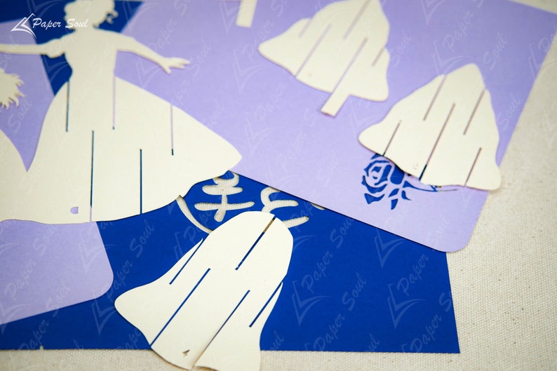 May include: White paper cutouts of a woman in a dress and several bells. The cutouts are on top of a blue and purple paper background with the text "Paper Soul" repeated on the background.