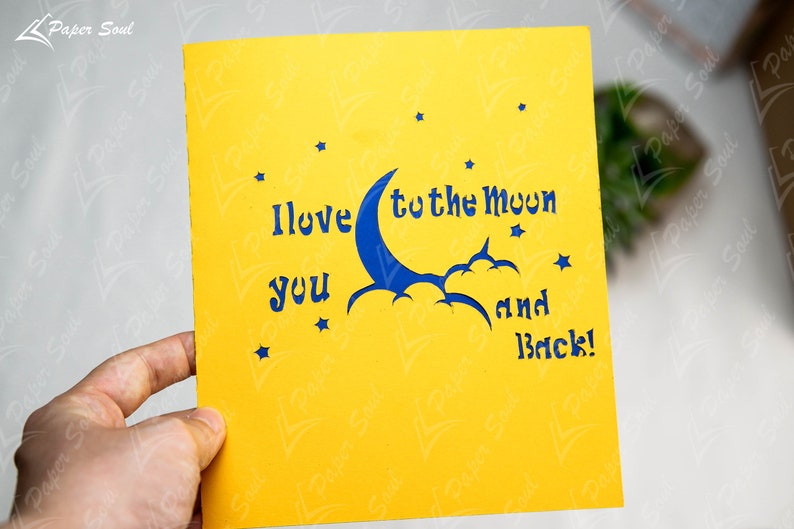May include: A yellow card with a blue crescent moon and stars cut out. The card reads "I love you to the moon and back!"