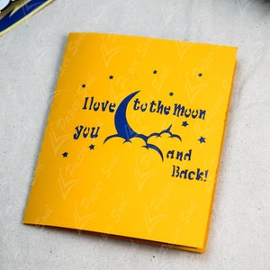 May include: A yellow card with a blue crescent moon and clouds, and the text "I love you to the moon and back!" with stars around the moon.