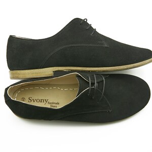 May include: A pair of black suede lace-up shoes with a brown leather sole. The shoes are handmade and have the brand name "Svonya" printed on the insole.