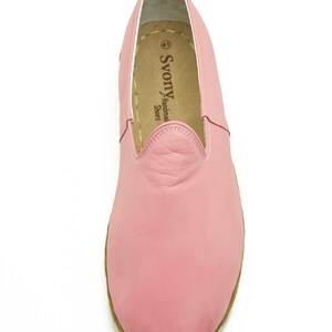 May include: A pair of pink leather slip-on shoes with a brown sole. The shoes have a simple design and are made by "SvonY Handmade Shoes".