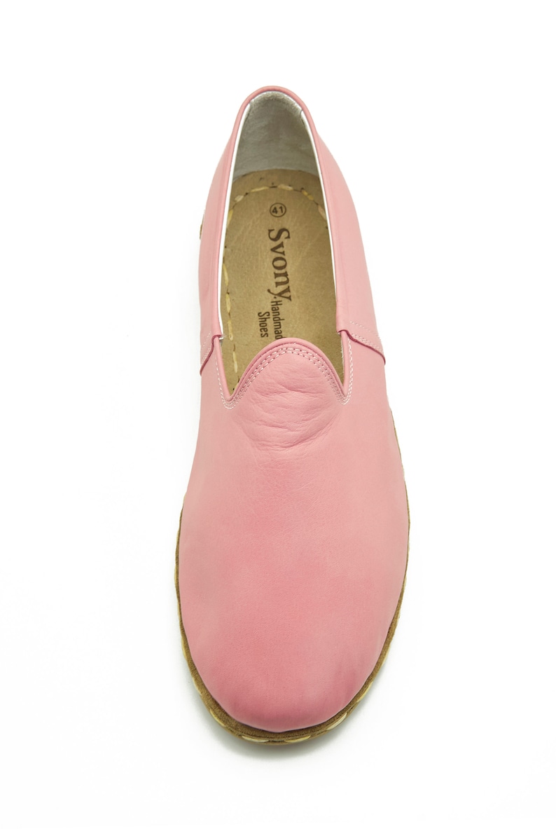 May include: A pair of pink leather slip-on shoes with a brown sole. The shoes have a simple design and are made by "SvonY Handmade Shoes".