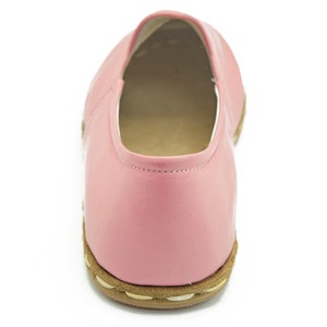 May include: A pair of pink leather slip-on shoes with a brown sole.