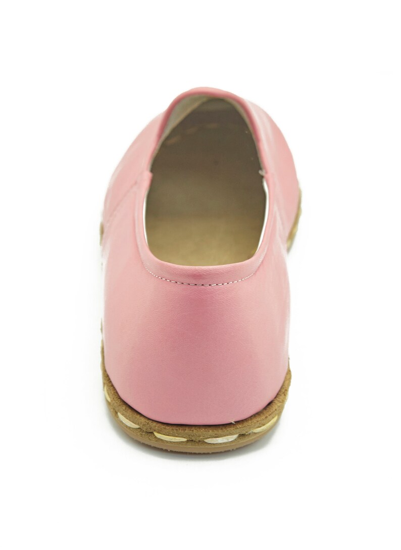 May include: A pair of pink leather slip-on shoes with a brown sole.
