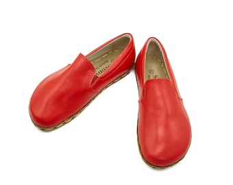 May include: A pair of red leather slip-on shoes with a slightly rounded toe. The shoes have a simple design and a comfortable look.