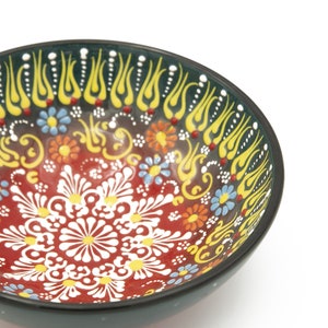 K&ouml;nnte beinhalten: Eine schwarze Sch&uuml;ssel mit einem farbenfrohen Blumendesign. Die Sch&uuml;ssel ist mit roten, gelben, blauen und wei&szlig;en Blumen und Spiralen verziert. Die Sch&uuml;ssel ist perfekt zum Servieren von Snacks oder Dips.