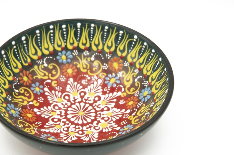 K&ouml;nnte beinhalten: Eine schwarze Sch&uuml;ssel mit einem farbenfrohen Blumendesign. Die Sch&uuml;ssel ist mit roten, gelben, blauen und wei&szlig;en Blumen und Spiralen verziert. Die Sch&uuml;ssel ist perfekt zum Servieren von Snacks oder Dips.